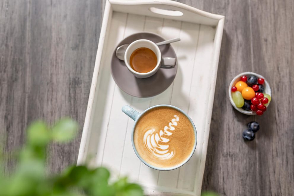 Milchkaffee und Espresso auf Tablett mit Obstschale daneben